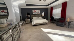 Un dormitorio moderno con una cama grande, un escritorio y una silla. Hay un aparador con cajones y un espejo.