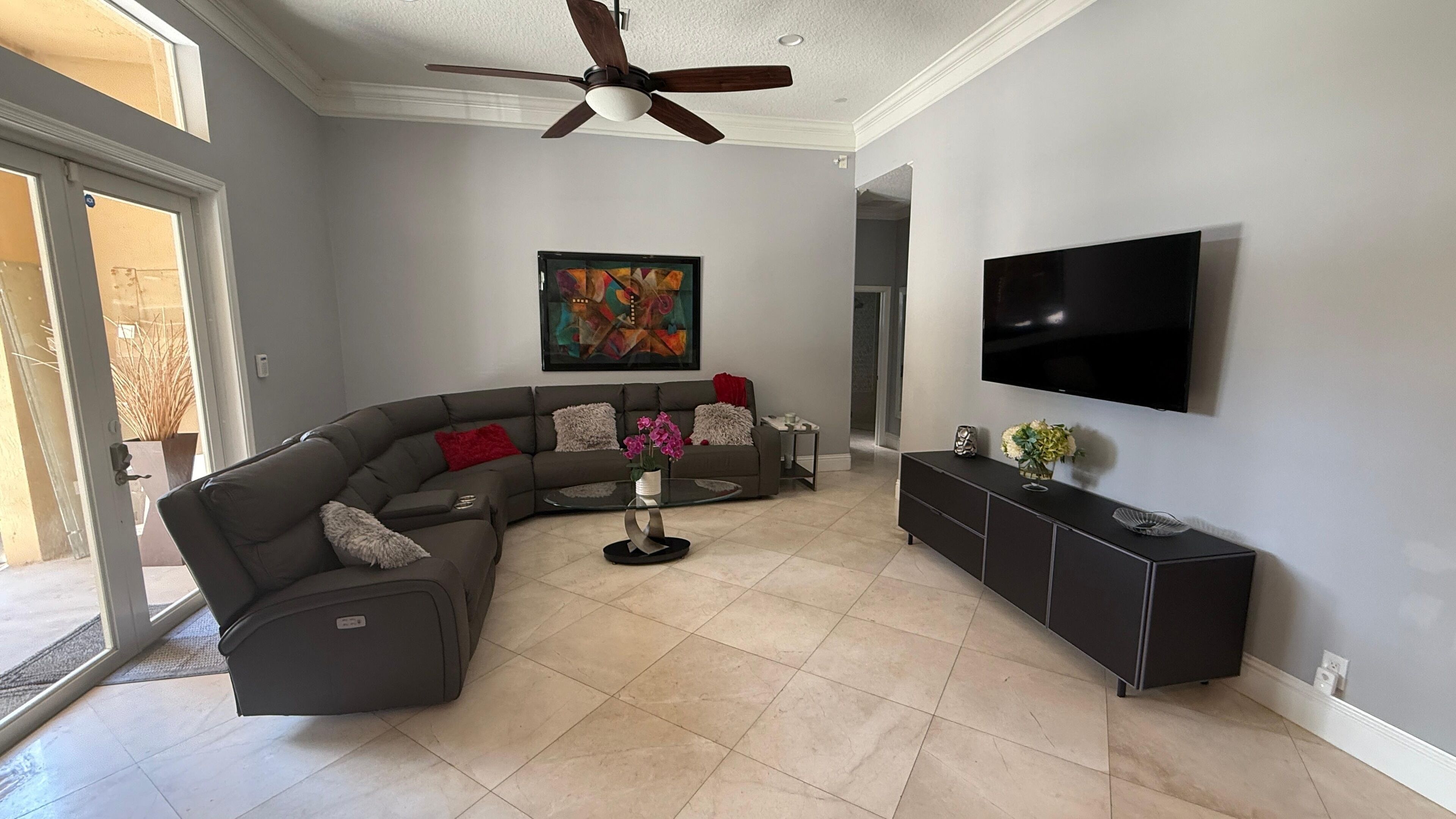 A modern living room with a sectional sofa, a flat-screen TV, and a ceiling fan.
