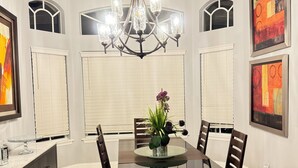 Comedor con mesa de vidrio, sillas de madera oscura, una lámpara de araña y obras de arte en las paredes.