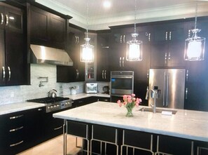 Una cocina moderna con armarios oscuros, electrodomésticos de acero inoxidable, encimera de mármol e iluminación colgante.