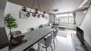 A modern living room with a dining area, a grey sofa, a flat-screen TV, and a large window.