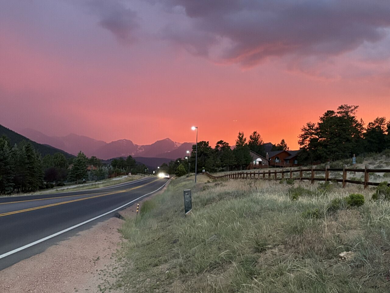 A road with a wooden fence on the right, leading to a house with a mountain backdrop.