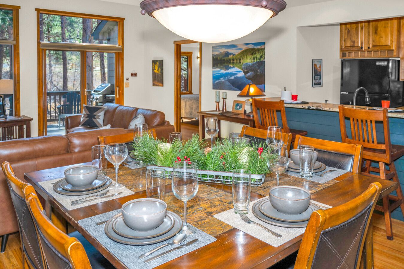 Een eethoek met een houten tafel voor vier personen, omringd door stoelen, met zicht op een keuken en een woonkamer op de achtergrond.