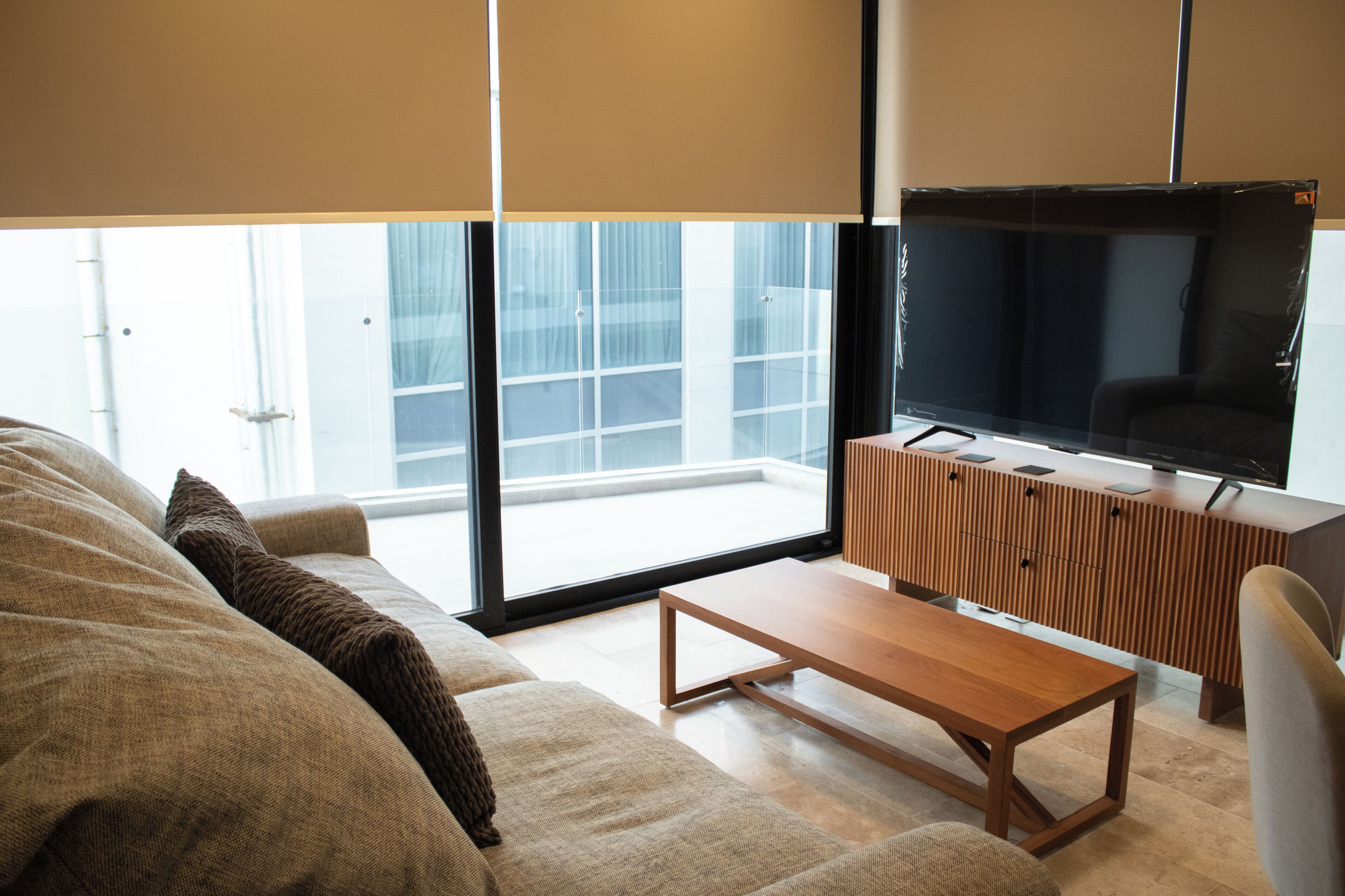 A modern living room with a sofa, a wooden coffee table, and a television on a wooden cabinet.