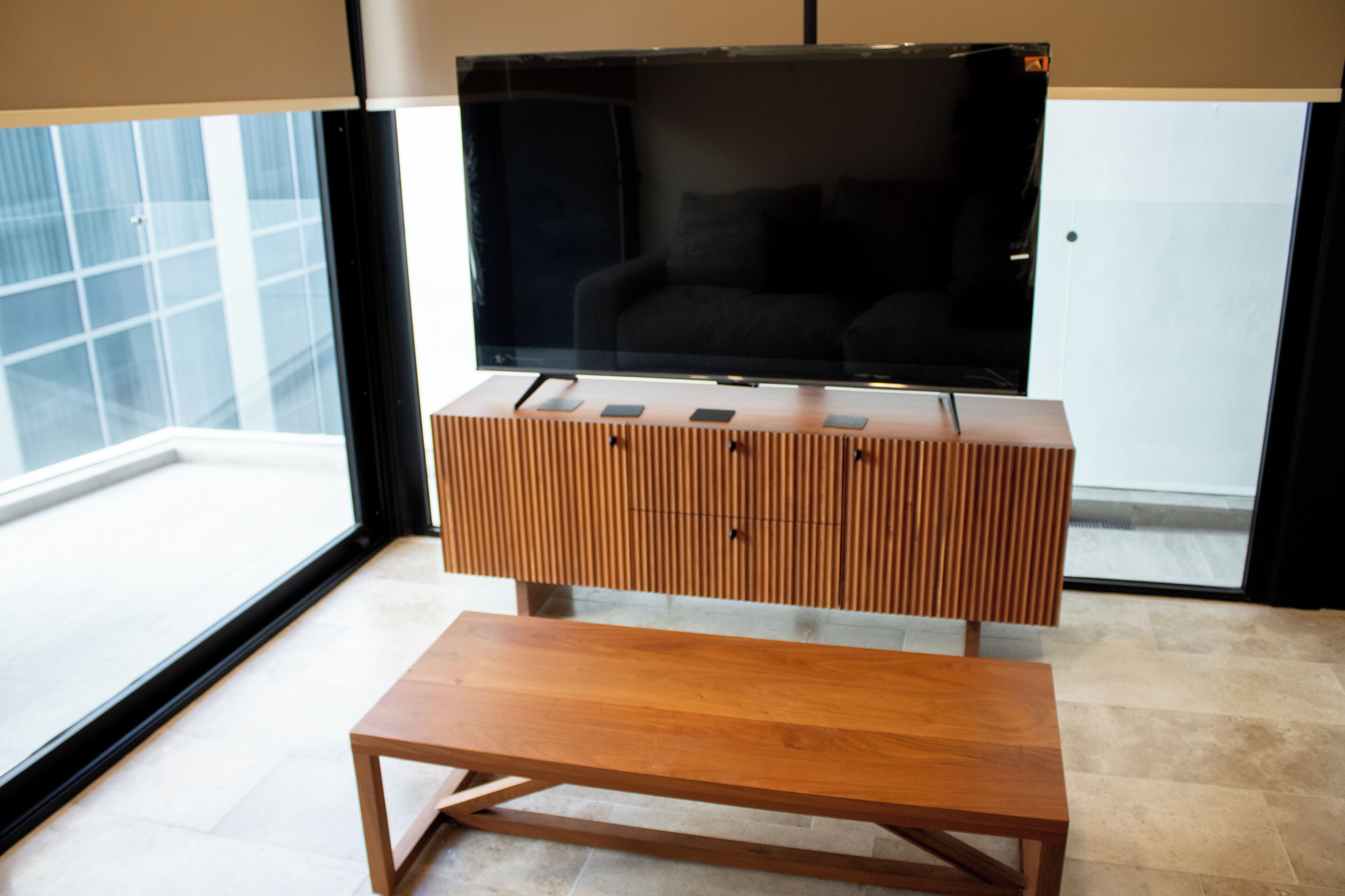 A modern living room with a wooden entertainment unit, a flat-screen TV, and a wooden bench.