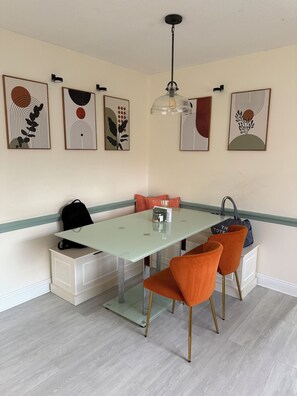 A dining area with a glass table, orange chairs, and artwork on the walls. - Spacious 2 BR + Sunroom - Near Beaches and Downtown (St. Petersburg)
