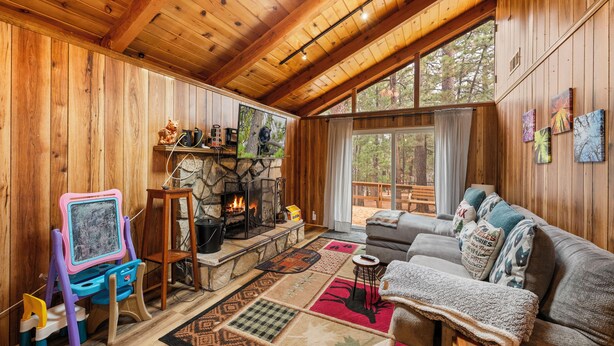 A cozy cabin interior with a stone fireplace, wooden walls, a large window, and a comfortable seating area. - Mama Bear's Cozy Cabin - Fireplace, Central Heat, Spacious Deck (Sugarloaf)