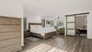 Une chambre à coucher avec un lit en bois, une table de chevet, une commode et une porte-fenêtre coulissante donnant sur une salle de bain.