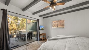 Une chambre avec un grand lit, un ventilateur de plafond, une porte-fenêtre coulissante donnant sur une terrasse et une petite table avec une chaise.