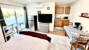 Quarto compacto com cama, escrivaninha, televisão, cozinha compacta e área de refeições.