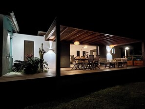 An outdoor dining area with a wooden deck, a dining table with chairs, and a hanging light fixture. - Villa le Paradis Secret: Ocean view, river access. (Goyave)