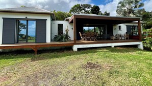 A modern house with a covered patio, large sliding doors, and a view of the ocean. - Villa le Paradis Secret: Sea view, river access. (Goyave)