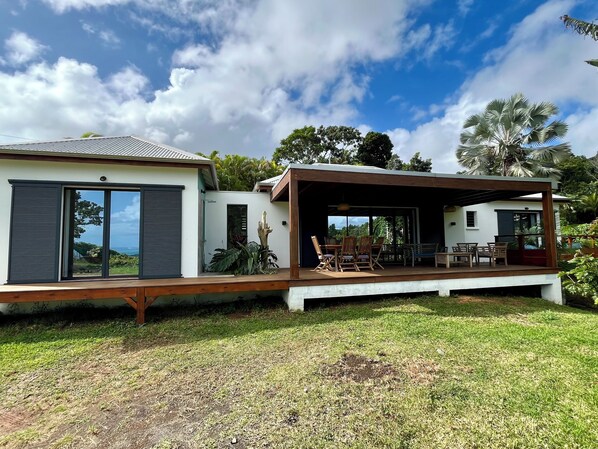 A modern house with a covered patio, large sliding doors, and a view of the ocean. - Villa le Paradis Secret: Ocean view, river access. (Goyave)