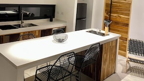 Une cuisine moderne avec un plan de travail blanc, des appareils électroménagers noirs et un plafond en bois.