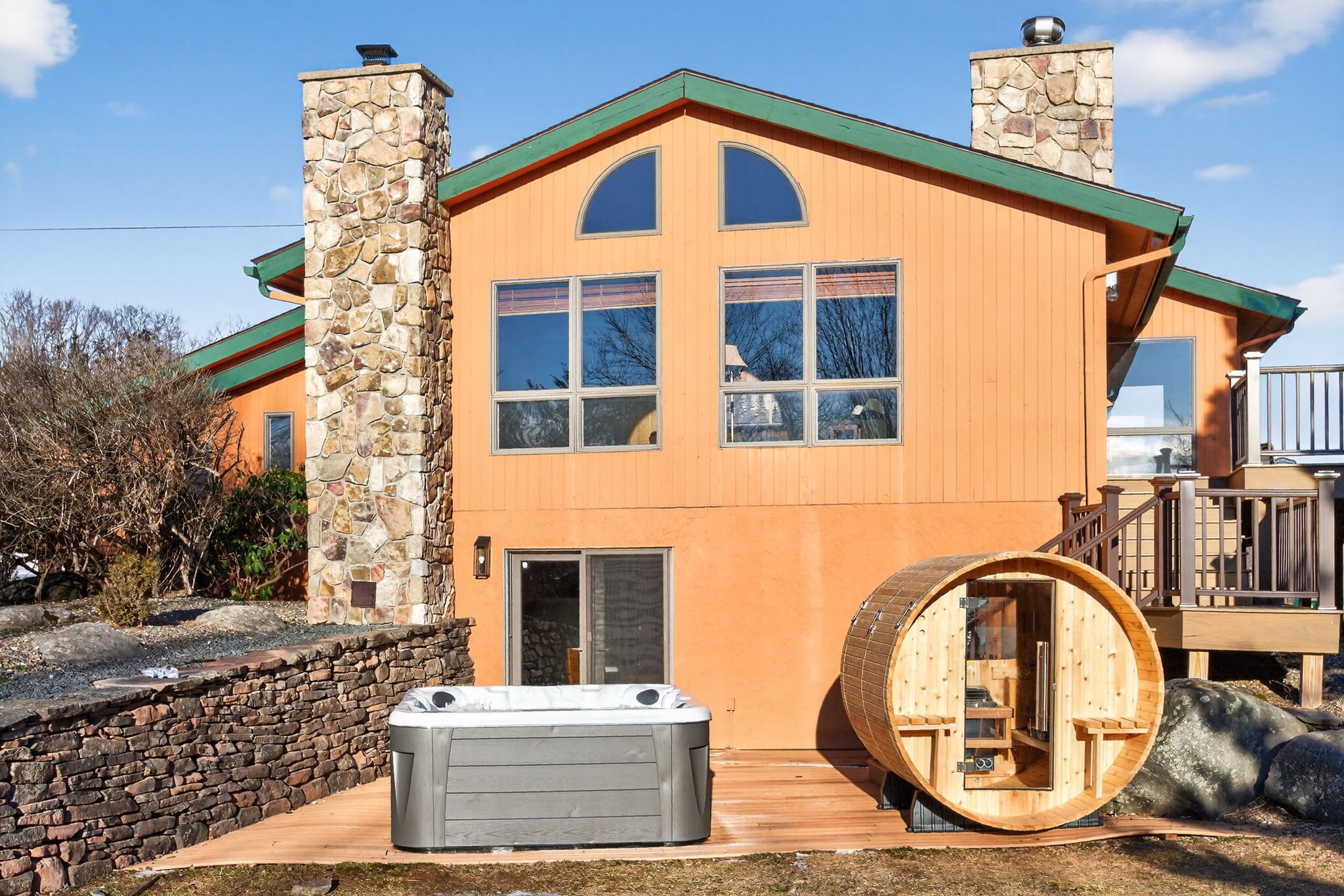A modern house with a stone chimney, a wooden deck, and a hot tub.