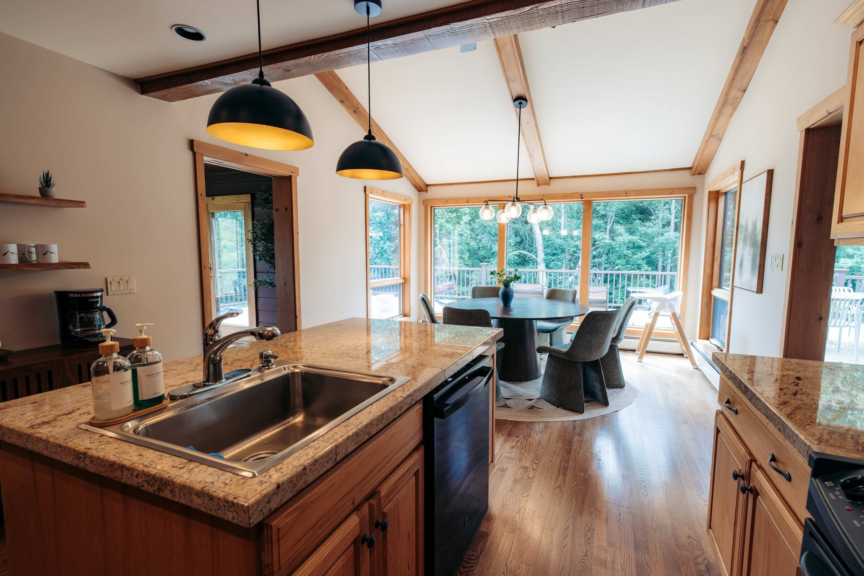 A modern kitchen with a central island, a dining area with a round table, and large windows offering a view of the outdoors.