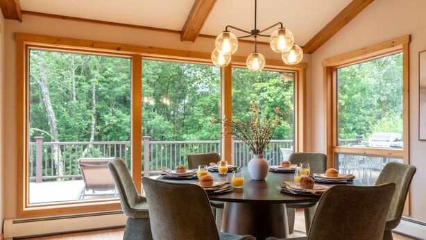 A dining area with a round table, chairs, and a view of a balcony with a railing. - Le View Chalet- HotTub, Sauna, Fire Pit, Geodome (Maplecrest)