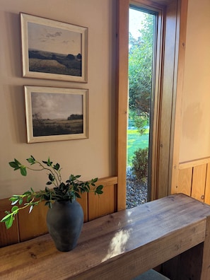 A wooden bench with a potted plant, two framed pictures on the wall, and a window with a view of greenery. - Le View Chalet- HotTub, Sauna, Fire Pit, Geodome (Maplecrest)