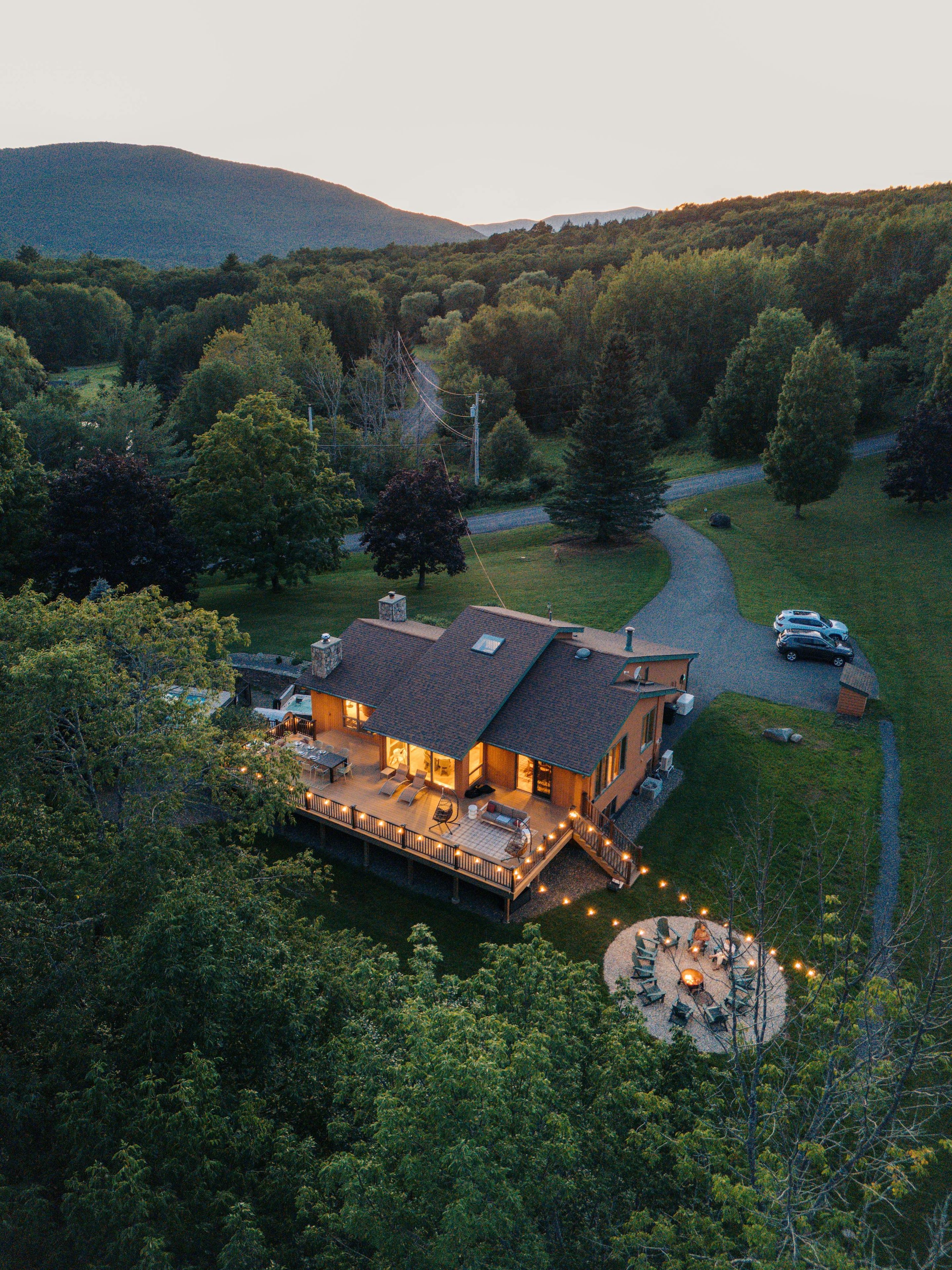 A large house with a deck, surrounded by trees and a hilly landscape.