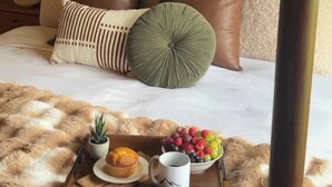 A bed with multiple pillows, a tray with food and a mug, and a lamp on a nightstand. - Le View Chalet- HotTub, Sauna, Fire Pit, Geodome (Maplecrest)