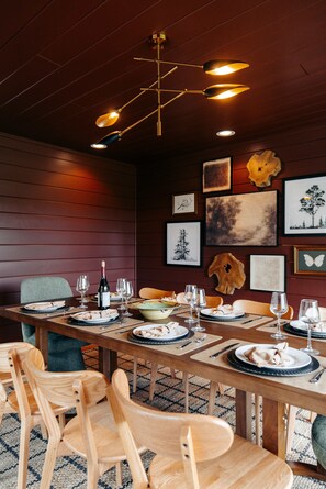A dining area with a long wooden table set for a meal, surrounded by wooden chairs.