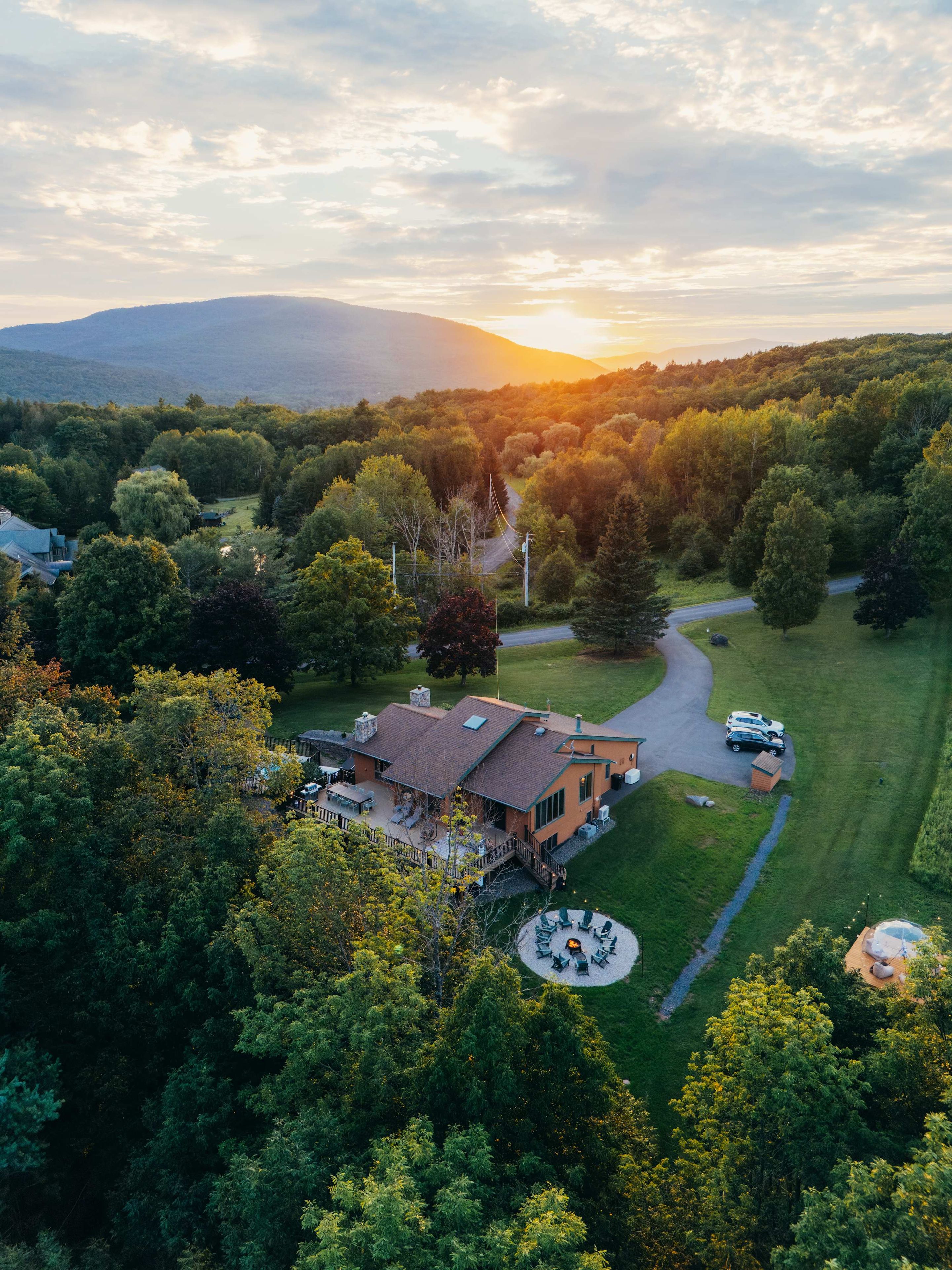 A large house with a spacious patio, surrounded by lush greenery and a winding driveway.