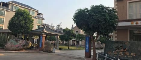 A gated entrance with a traditional pavilion, a large stone monument, and a building with a flag.