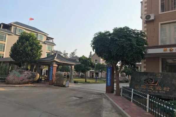 A gated entrance with a traditional pavilion, a large stone monument, and a building with a flag.