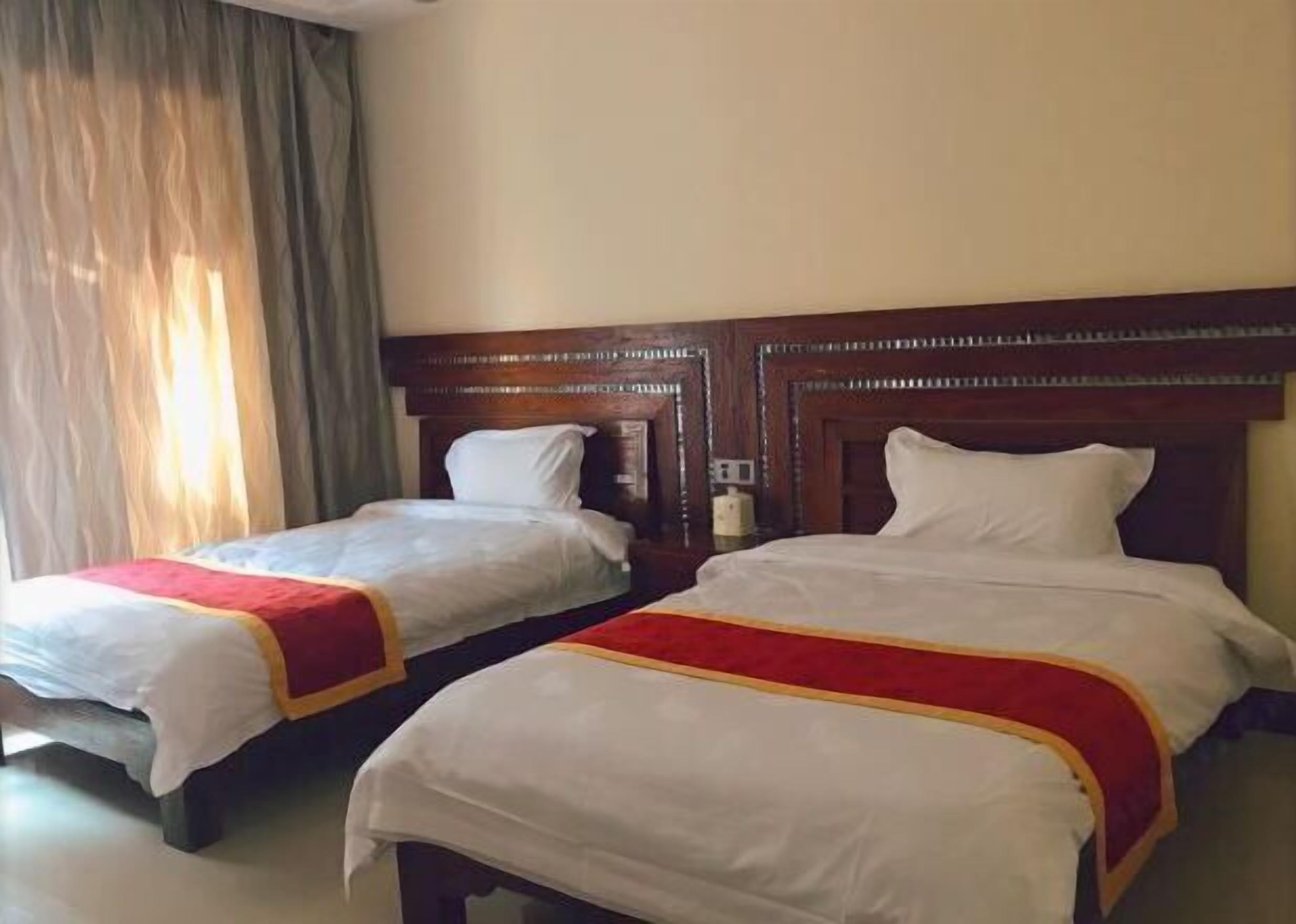 A hotel room with two beds, each with a wooden headboard, white bedding, and a red and yellow striped blanket.
