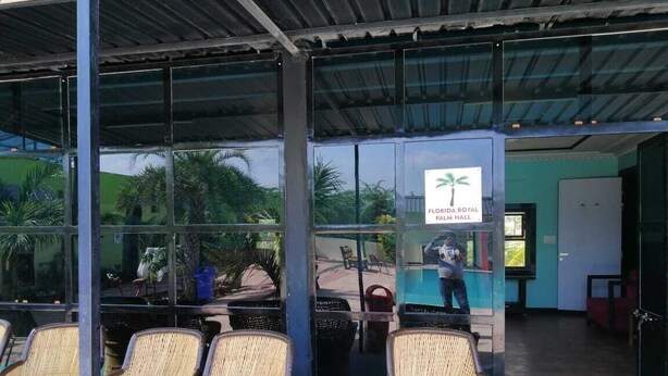 Un área de estar techada con sillas de mimbre, un letrero que indica Florida Royal Palm Hall y vistas al área de la piscina.