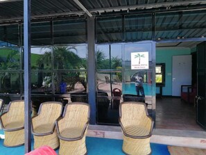 Un área de estar techada con sillas de mimbre, un letrero que indica Florida Royal Palm Hall y vistas al área de la piscina.