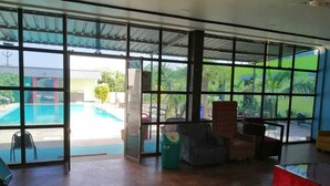 Una habitación amplia con ventanas grandes, una piscina visible a través del vidrio y un sofá rojo.