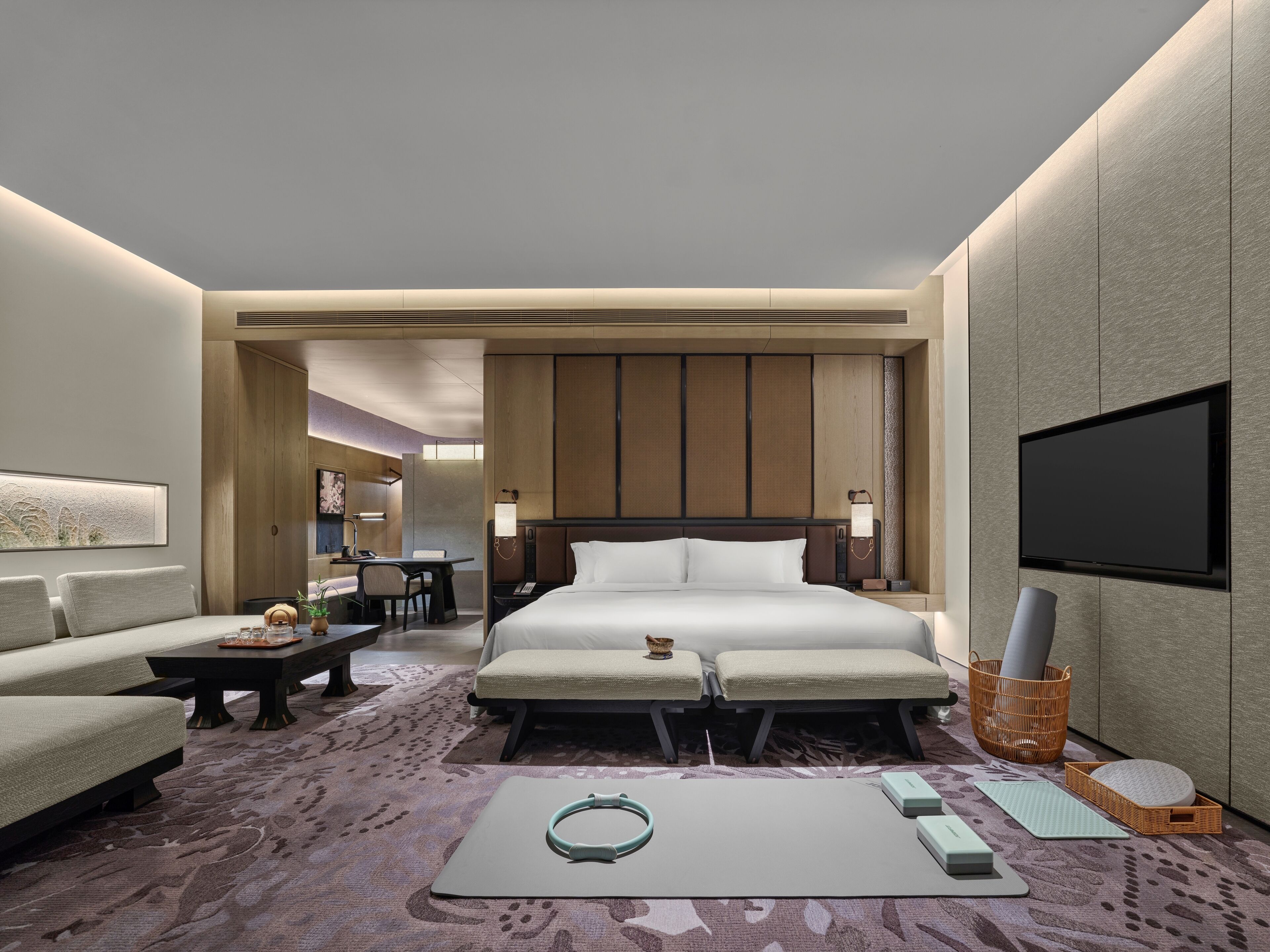 A modern hotel room with a large bed, a desk, a sofa, a TV, and a workout mat.