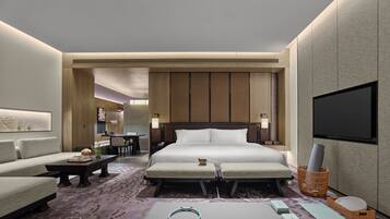 A modern hotel room with a large bed, a desk, a sofa, a TV, and a workout mat.