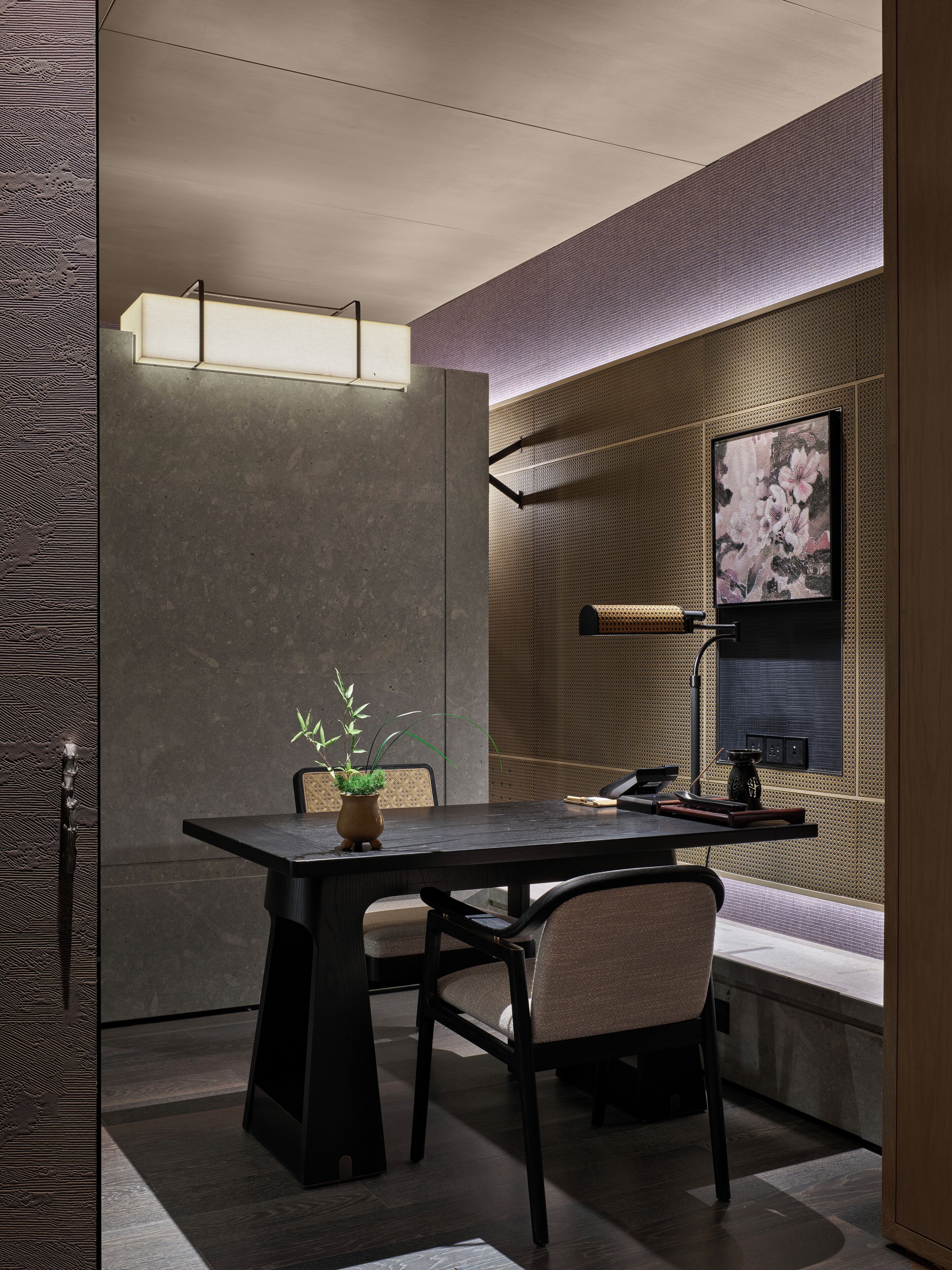 Un interior moderno con una mesa de madera oscura, sillas, una planta en maceta y una lámpara de pared.