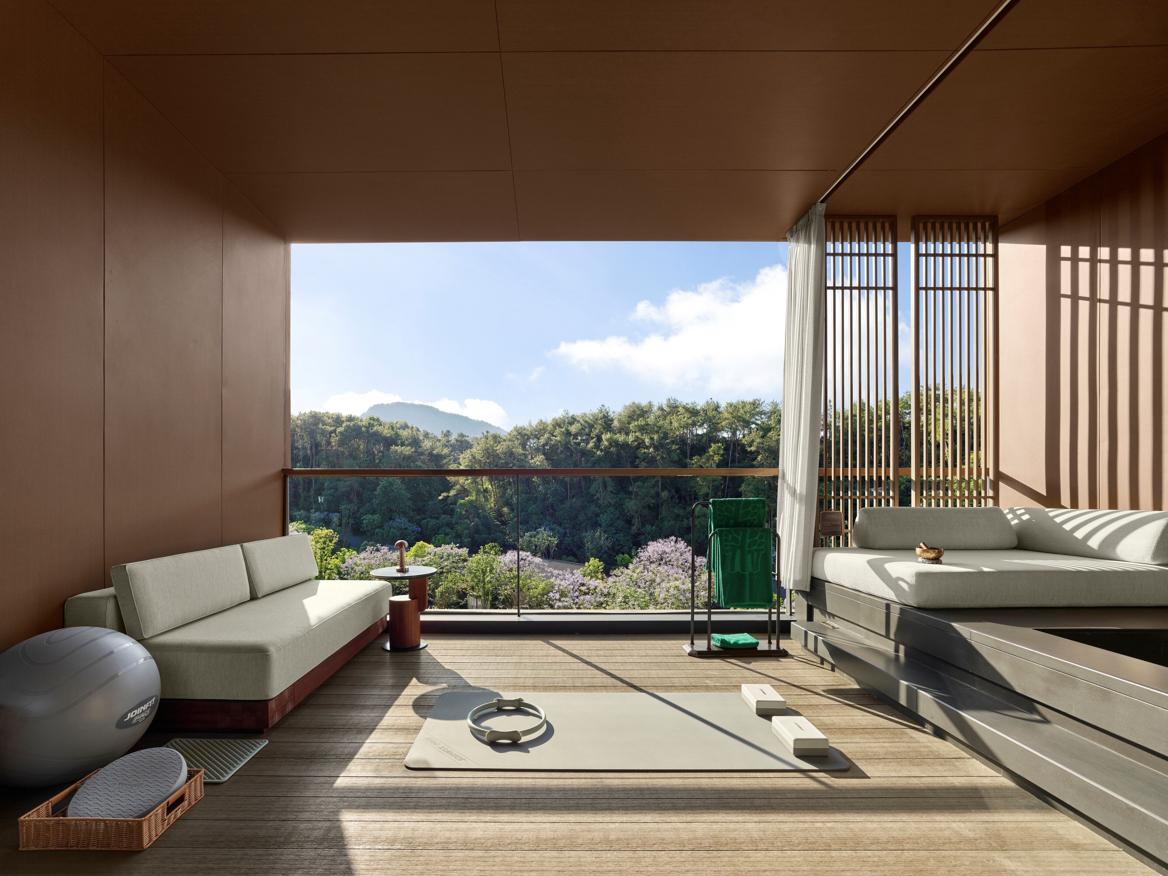 Un balcón moderno con sofá, equipo de ejercicio y vistas a una zona boscosa.
