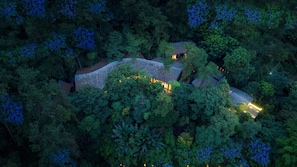Une vue aérienne d’un domaine isolé, recouvert d’arbres, comprenant plusieurs bâtiments, des allées illuminées et une structure centrale dotée d’un toit distinctif.
