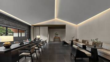 A modern interior with a long reception desk, seating area, and a view of a tree outside.