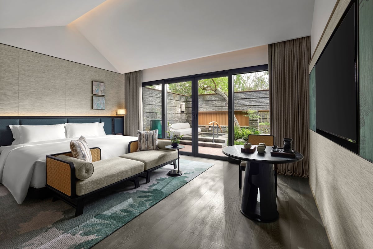 Habitación de hotel moderna con cama, sofá, mesa y vistas al exterior.