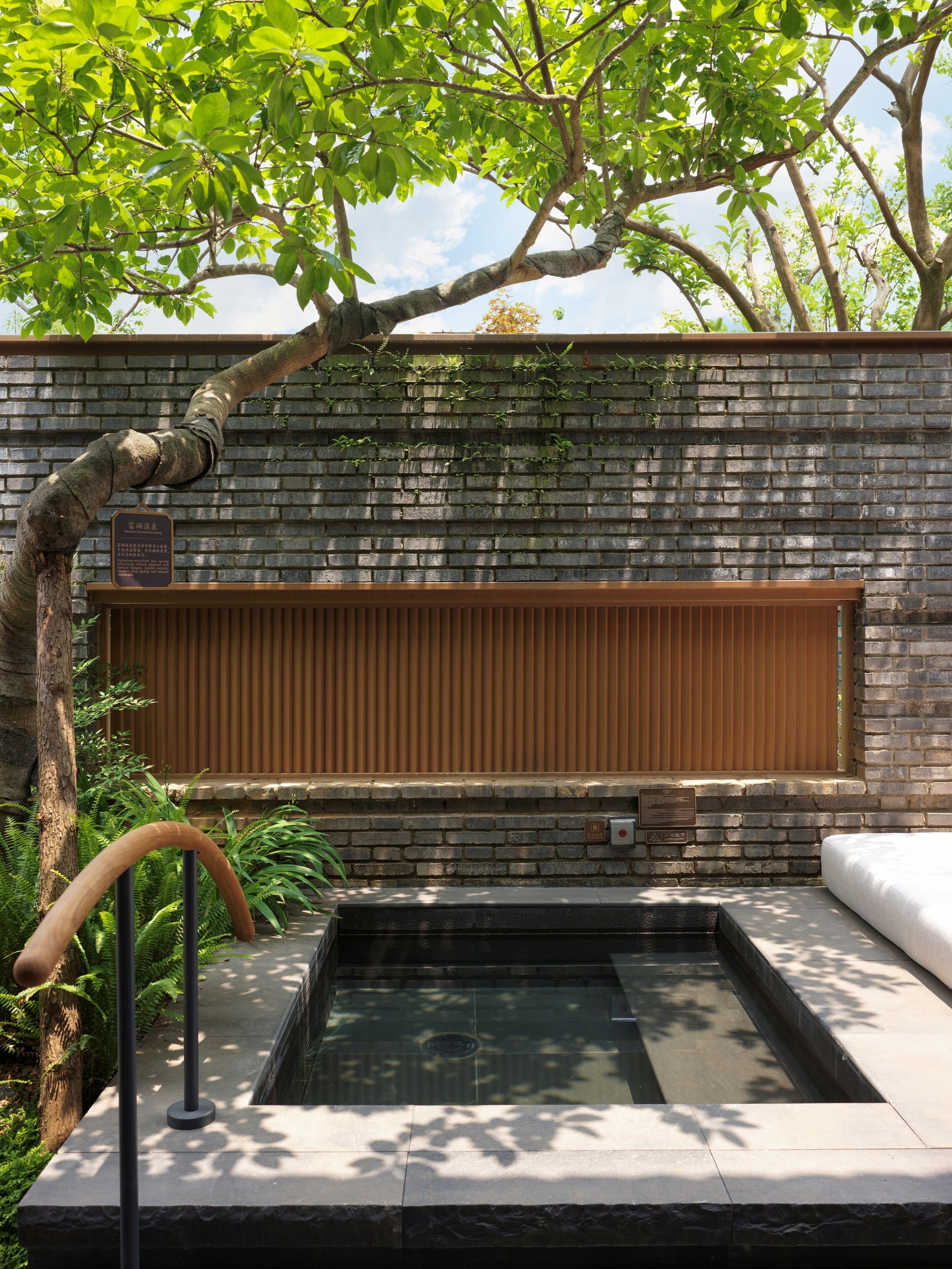 A spa area with a brick wall, a wooden slatted window, and a stone hot tub.