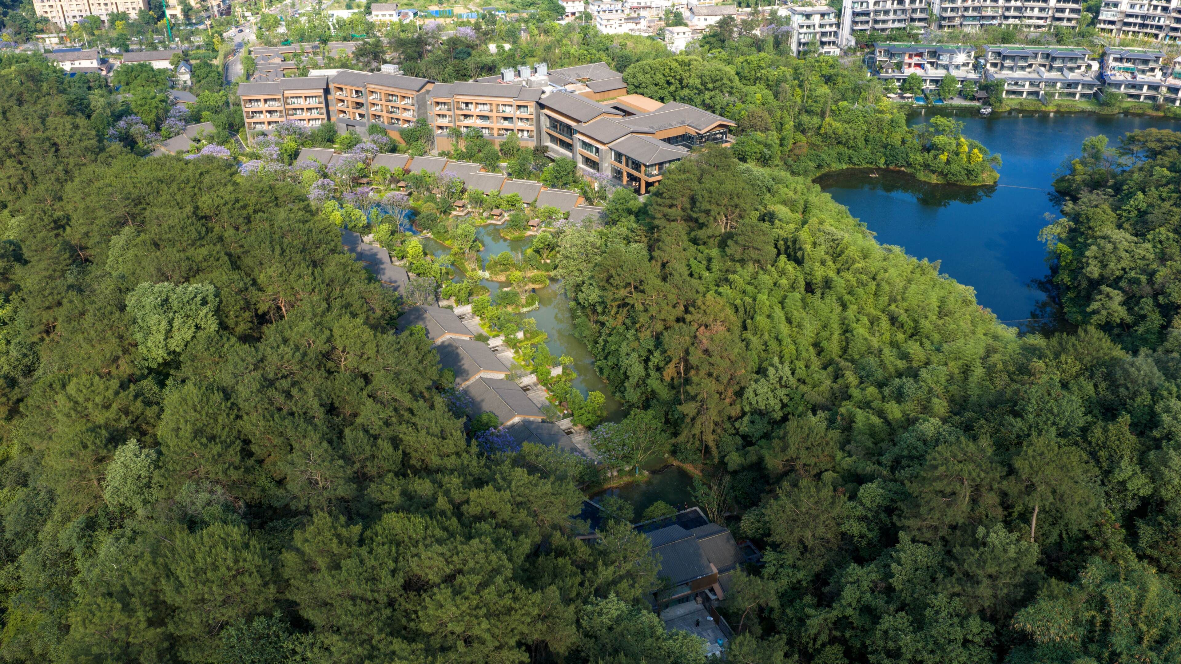 An aerial view of a hotel with multiple buildings, surrounded by dense forest and a lake.