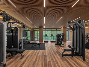 A modern gym with wooden flooring, exercise equipment, and large windows offering a view of greenery. - Banyan Tree Mount Emei (Leshan)