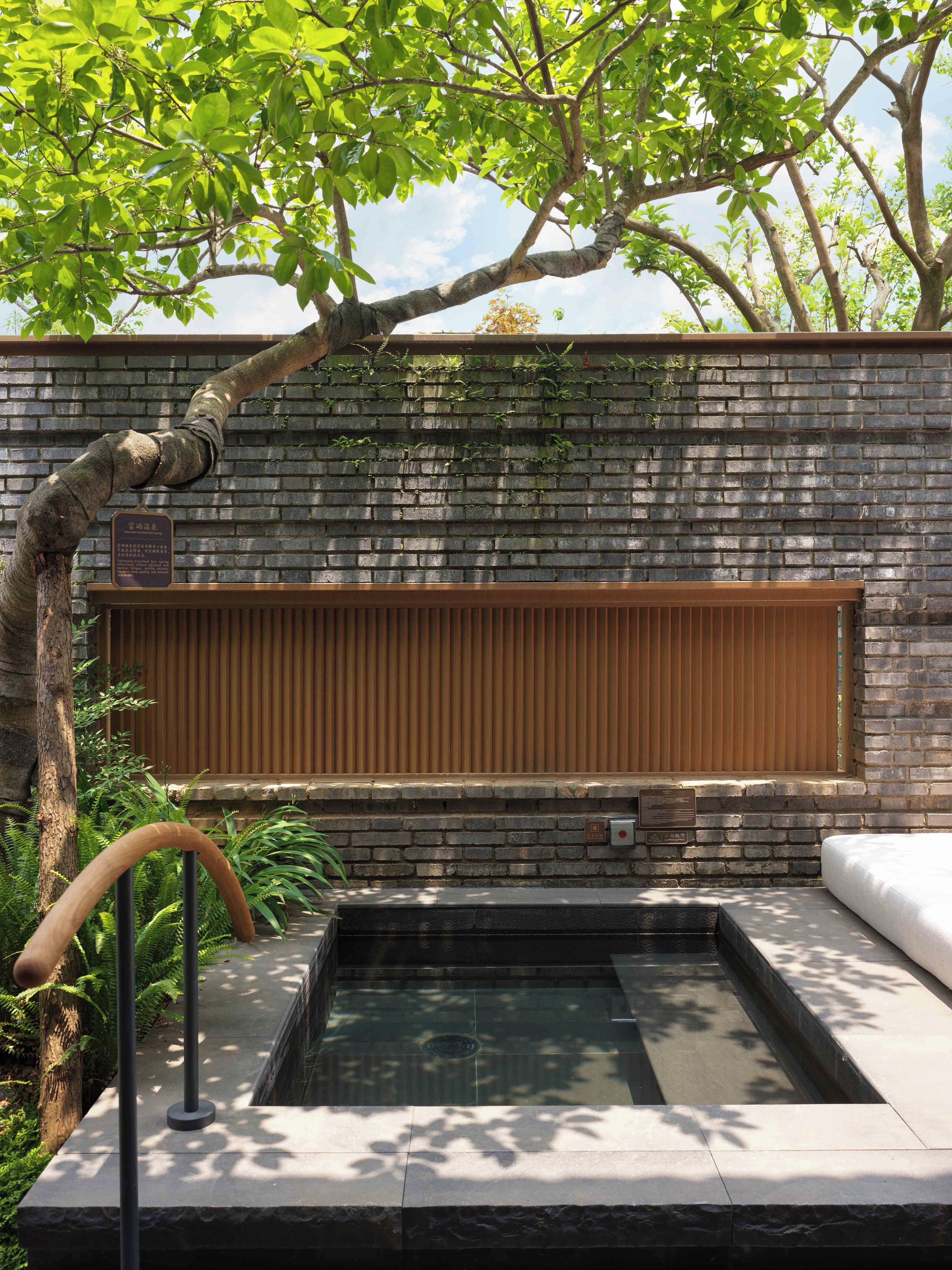 A spa area with a brick wall, a wooden bench, and a hot tub.