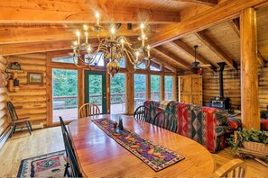 Ein Holzblockhaus-Interieur mit Esstisch, Stühlen, einem gemusterten Teppich, einer Couch und einer Kandelaber.