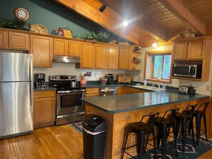 A kitchen with wooden cabinets, stainless steel appliances, a large island with bar stools, and a window with a view. - Bearview Lodge Alma Colorado (Fairplay)