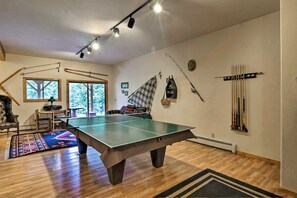 A room with a ping pong table, a chair, a couch, a fireplace, and a window. - Bearview Lodge Alma Colorado (Fairplay)