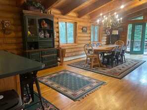 A wooden cabin interior with a dining table, chairs, a chandelier, and a cabinet with decorative items. - Bearview Lodge Alma Colorado (Fairplay)