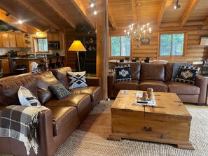 Ein gemütliches Blockhauss-Interieur mit einem braunen Ledersofa, einem Holztisch und einer Chandelüster.