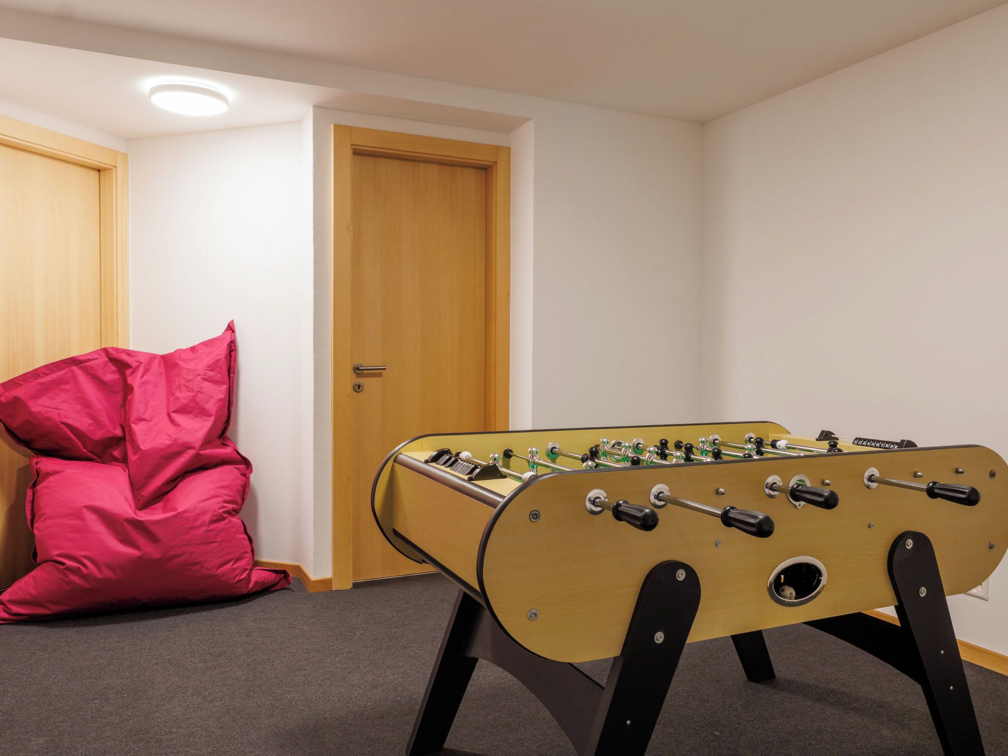 A room with a foosball table, a red bean bag chair, and a wooden door.