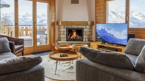Una sala de estar acogedora con chimenea, televisión y vistas a montañas nevadas a través de amplias ventanas.